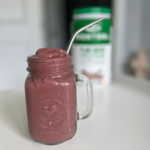 A mason jar mug is filled to the top with a thick and creamy protein shake.