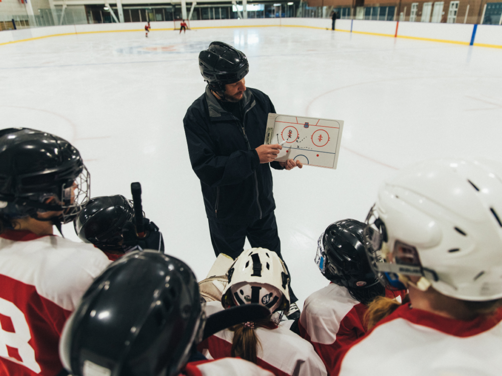 Hockey coach drawing out a drill on a coaching board while players look on. 